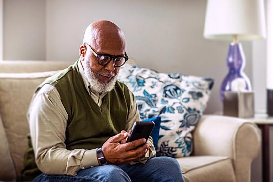 An elder person sits on a couch and uses a smartphone